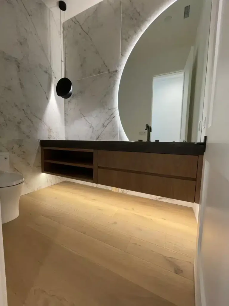 Modern bathroom with marble walls, floating wood vanity, backlit mirror, and elegant pendant light by basement contractor.