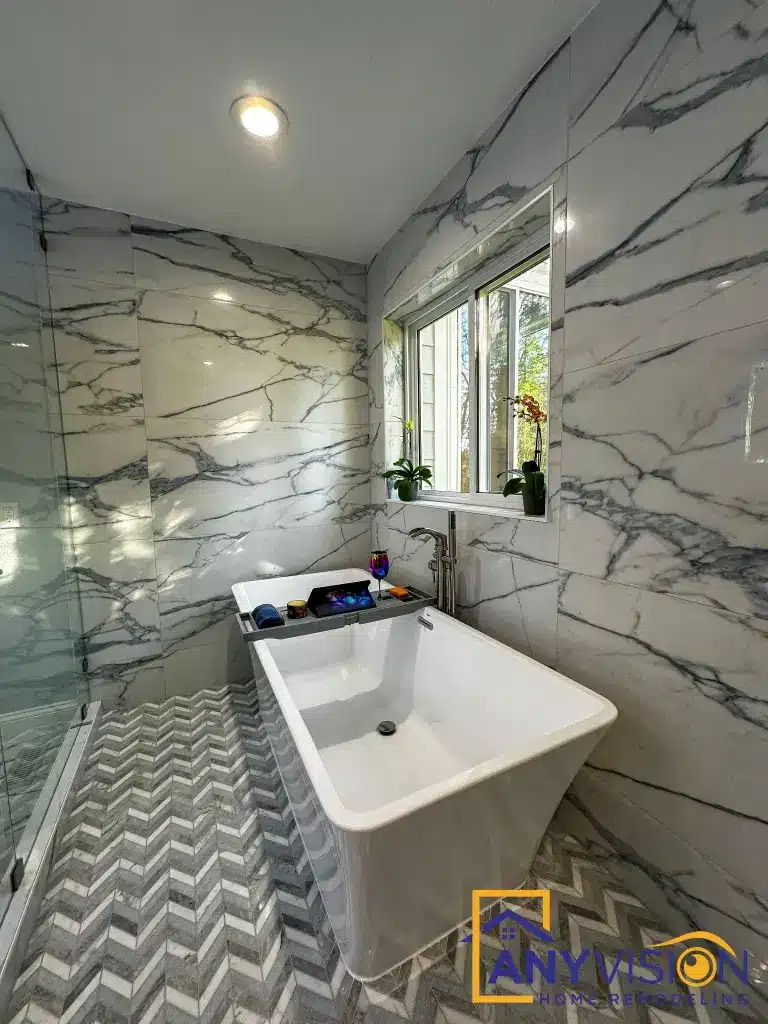 Freestanding tub set against the book-matched slab wall beneath a window