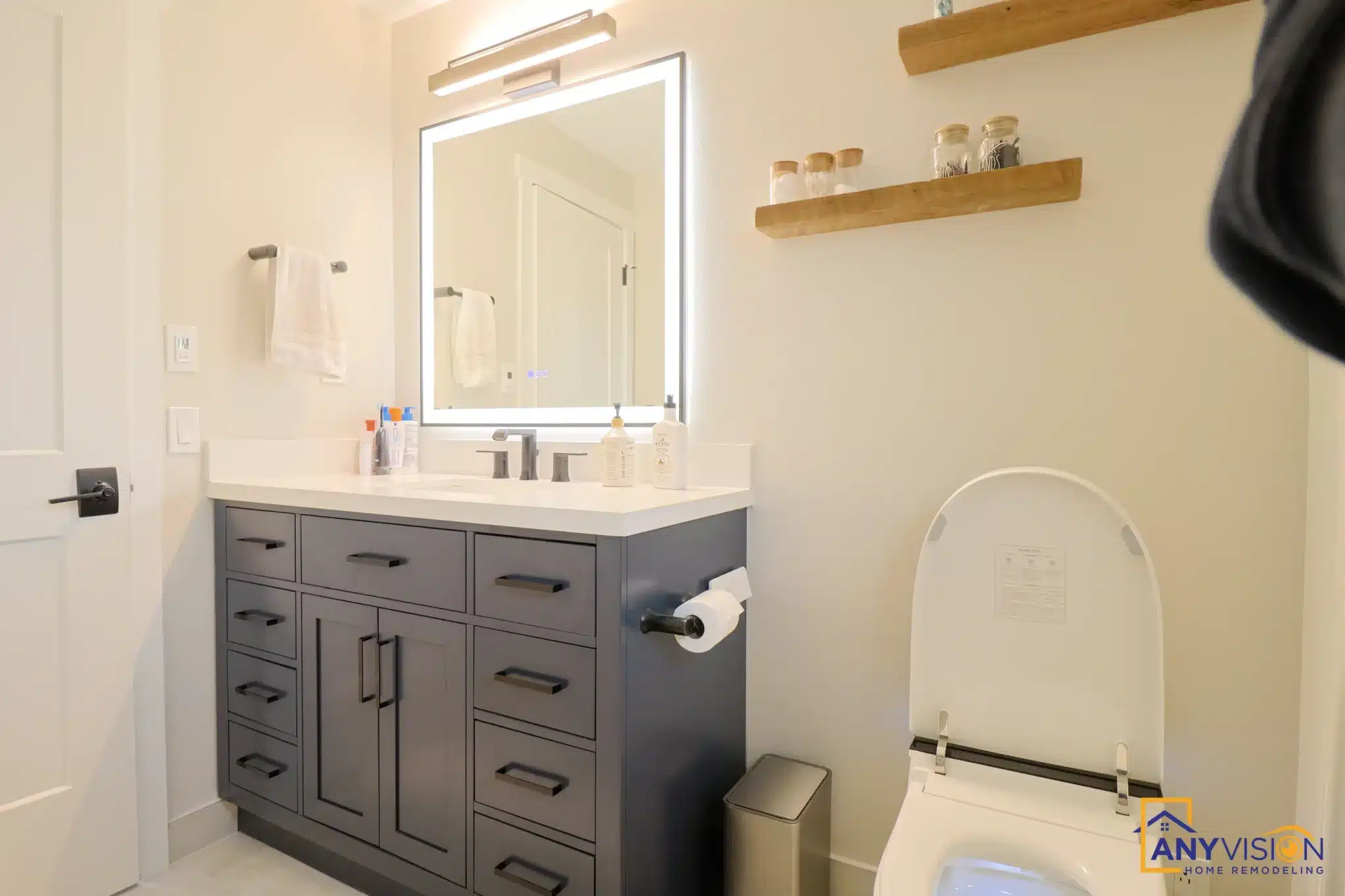 Second bathroom with a dark vanity, backlit mirror and oak shelving