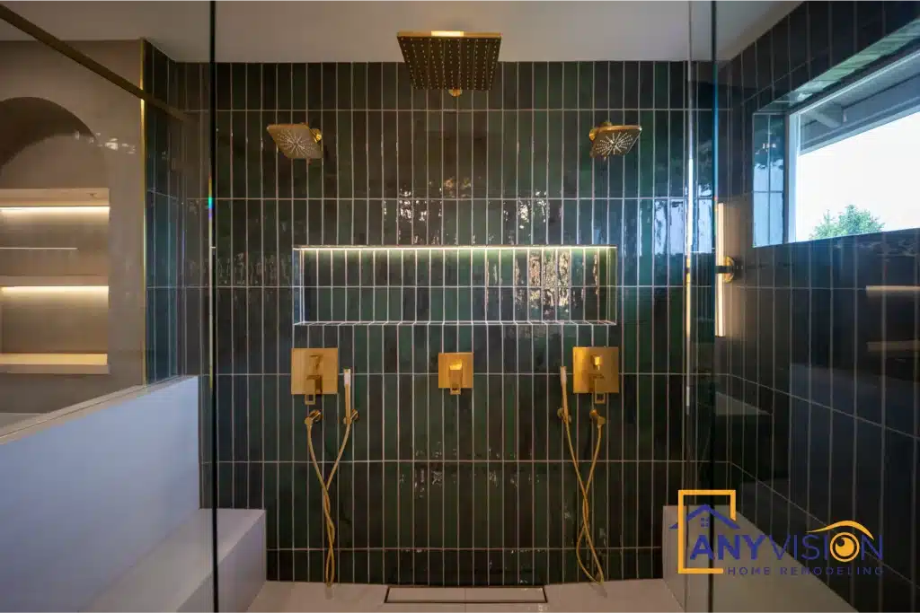 Twin shower heads and brass controls against vertically stacked dark green tile