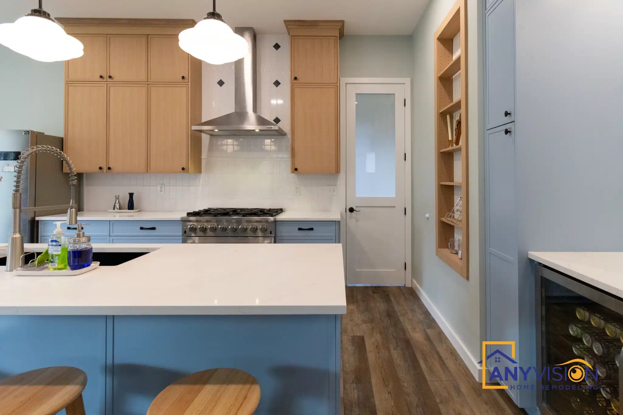 Natural wood upper cabinets above pale blue base cabinets and a white counter