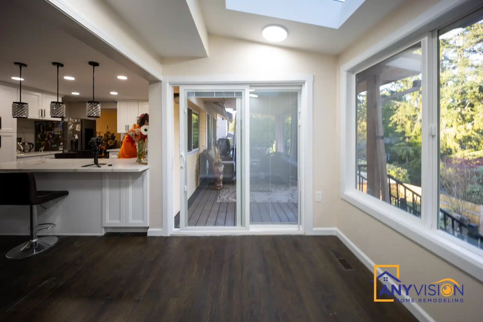 Glazed sunroom with dark plank flooring opening off the kitchen