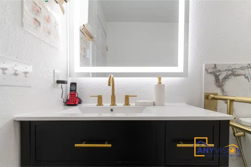 Wall-hung dark vanity with brass tapware and backlit mirror above