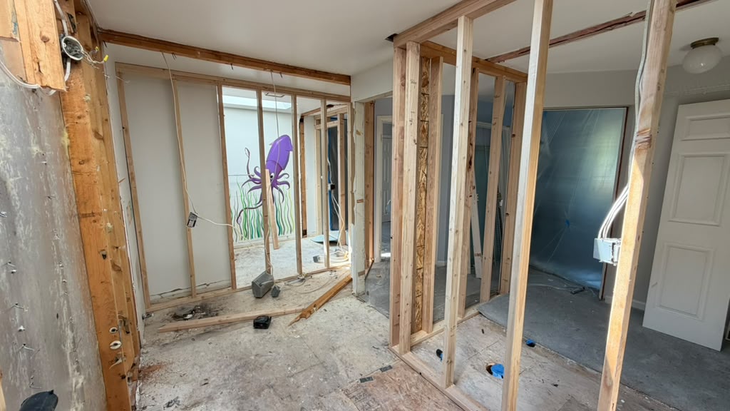 Stud framing exposed beside the remnant wall mural in a Redmond split-level