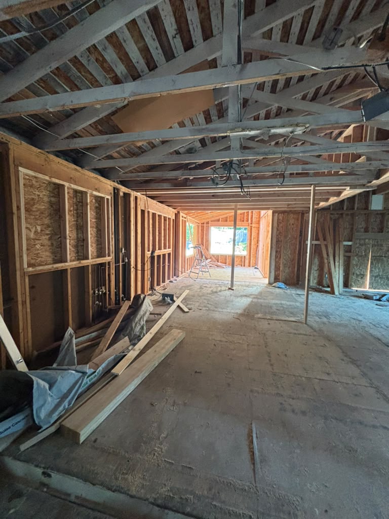 New room addition under construction in Redmond showing subflooring, open wall studs and insulated cavities beneath exposed roof framing