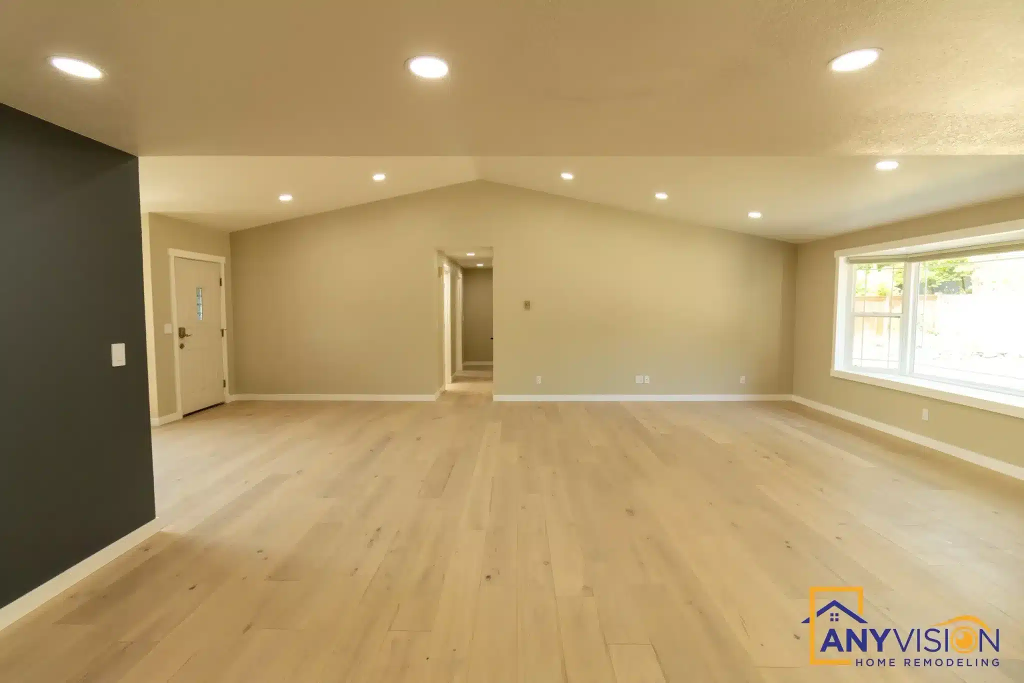 Empty basement with light wood flooring, cream walls, vaulted ceiling with recessed lights, and large windows.