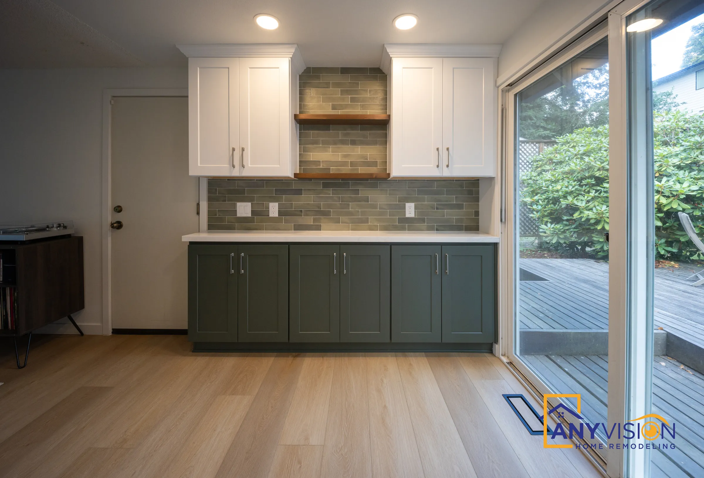 Coffee station with green base cabinets, tile backsplash and a walnut shelf beside the deck doors