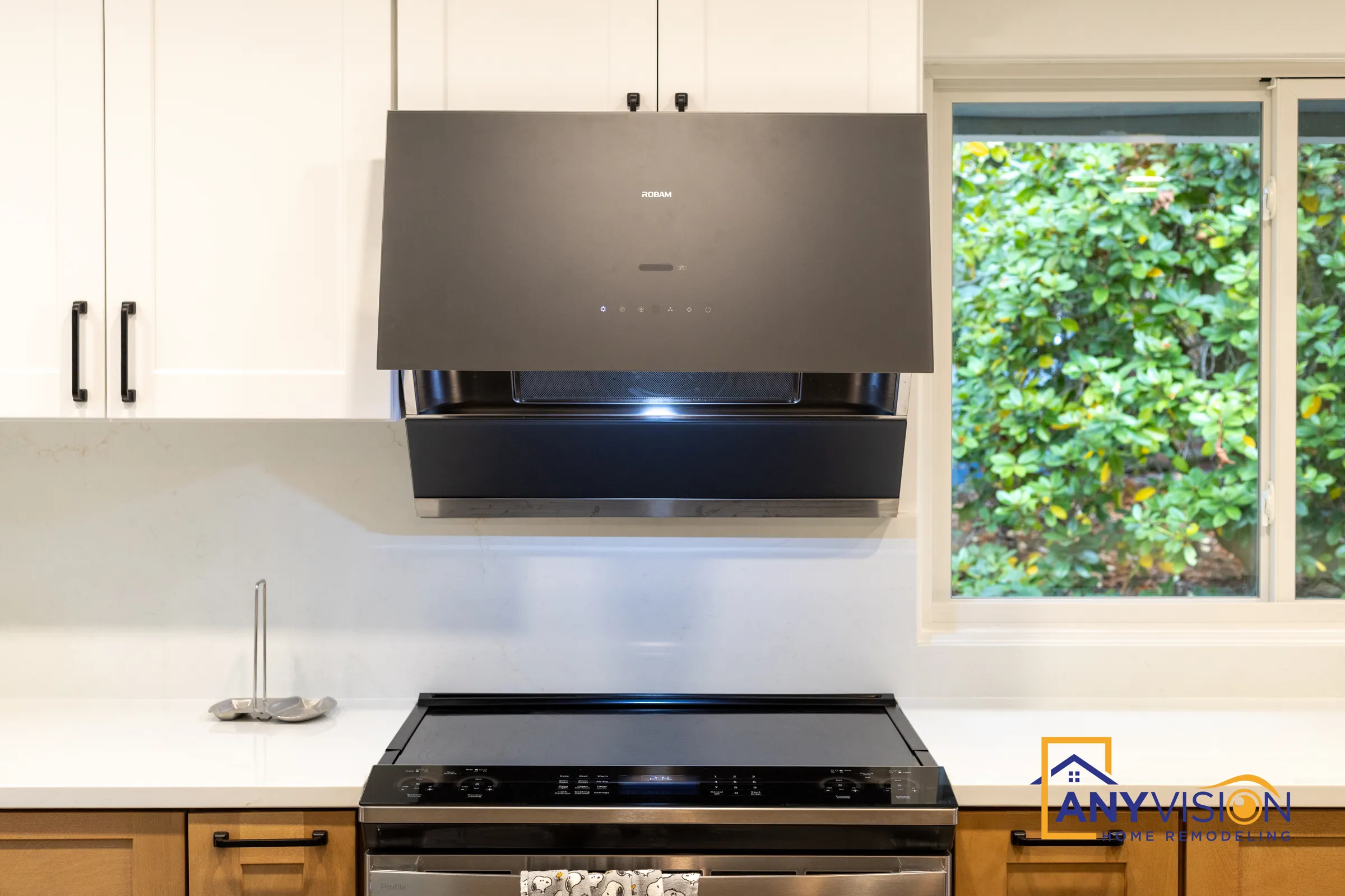 Black angled range hood over a white backsplash beside a garden window