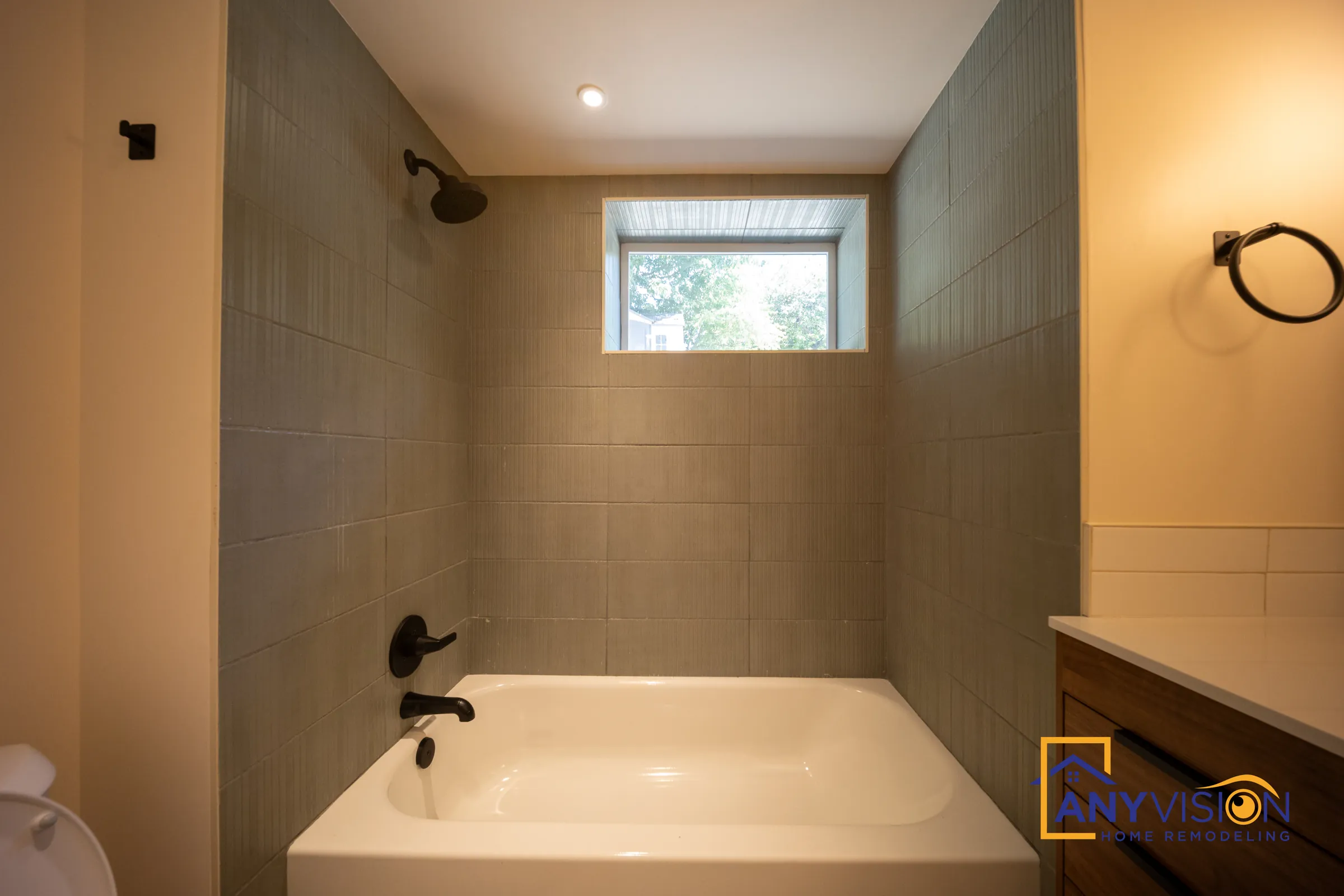 Green tile tub surround with matte black fixtures under a window