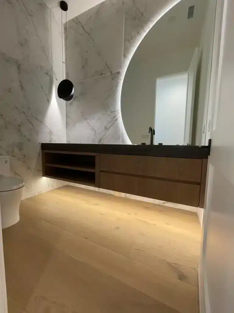 Modern bathroom with marble walls, floating wood vanity, backlit mirror, and elegant pendant light by basement contractor.